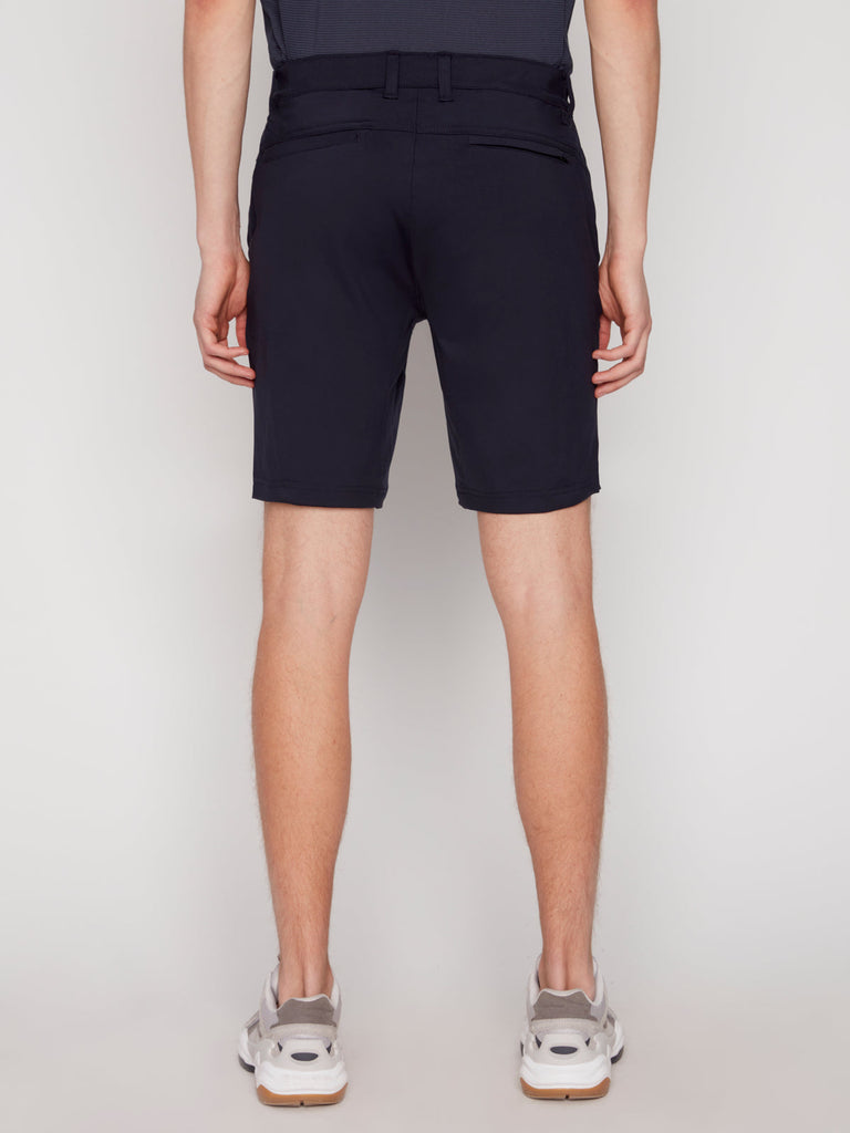 Back view of a person wearing Projek Raw DAMIAN MENS SHORT - NAVY and a dark shirt with white sneakers, standing against a plain light background.