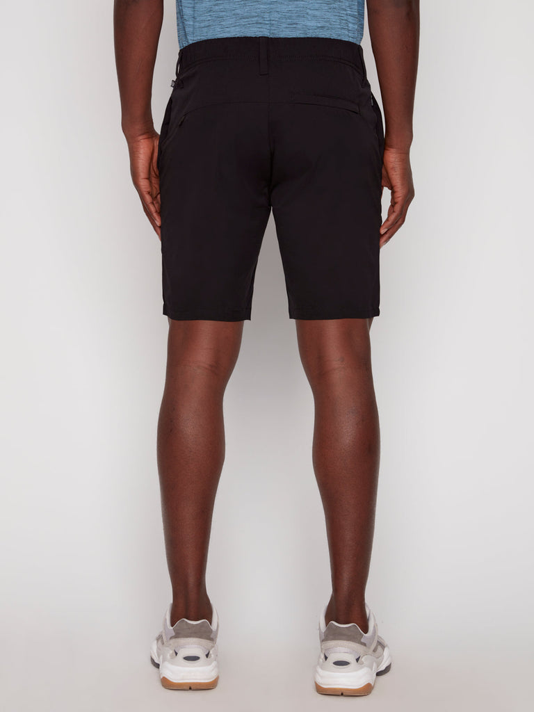 A person stands facing away from the camera against a plain white background, wearing Projek Raws ANTHONY MENS SHORT - BLACK, a blue shirt, and white sneakers.