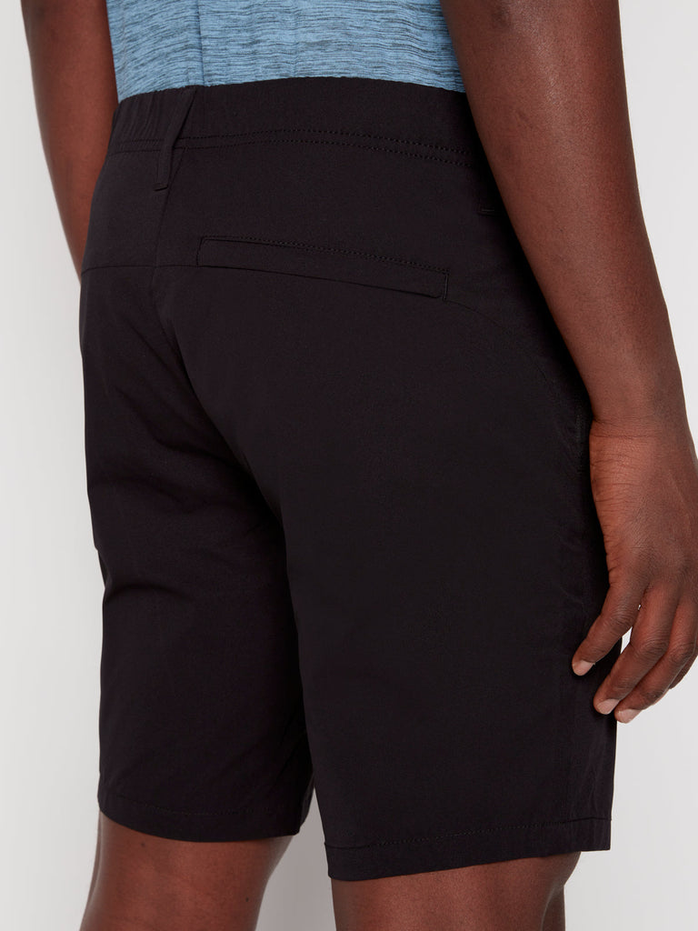 A person is shown from the back, waist down, wearing Projek Raw ANTHONY MENS SHORT - BLACK with a back welt pocket and a blue shirt, their right hand relaxed by their side.