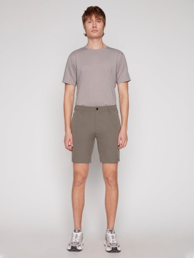 A person stands facing forward against a plain white background, wearing a light gray T-shirt, white sneakers, and ANTHONY MENS SHORT - MOSS by Projek Raw.