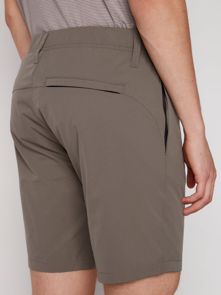 A person wearing Projek Raws ANTHONY MENS SHORT in Moss, featuring a back welt pocket and side pockets, is photographed from behind at waist level with their arm resting beside their body.