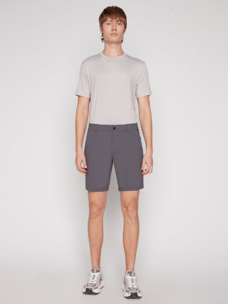 A person stands facing forward against a plain white background, wearing a light gray short-sleeve t-shirt, Projek Raw PAUL MENS SHORT - GREY, and white athletic shoes.