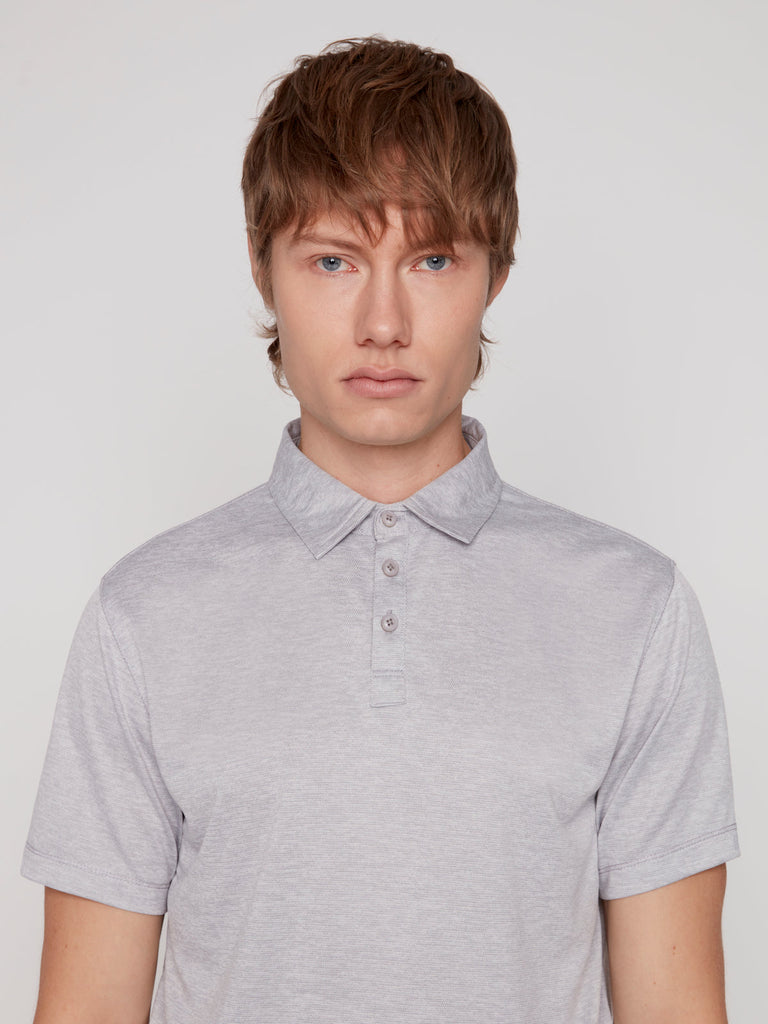 A young person with light brown hair and blue eyes wears the Projek Raw MICHAEL MENS POLO in light grey, looking directly at the camera against a plain light background.