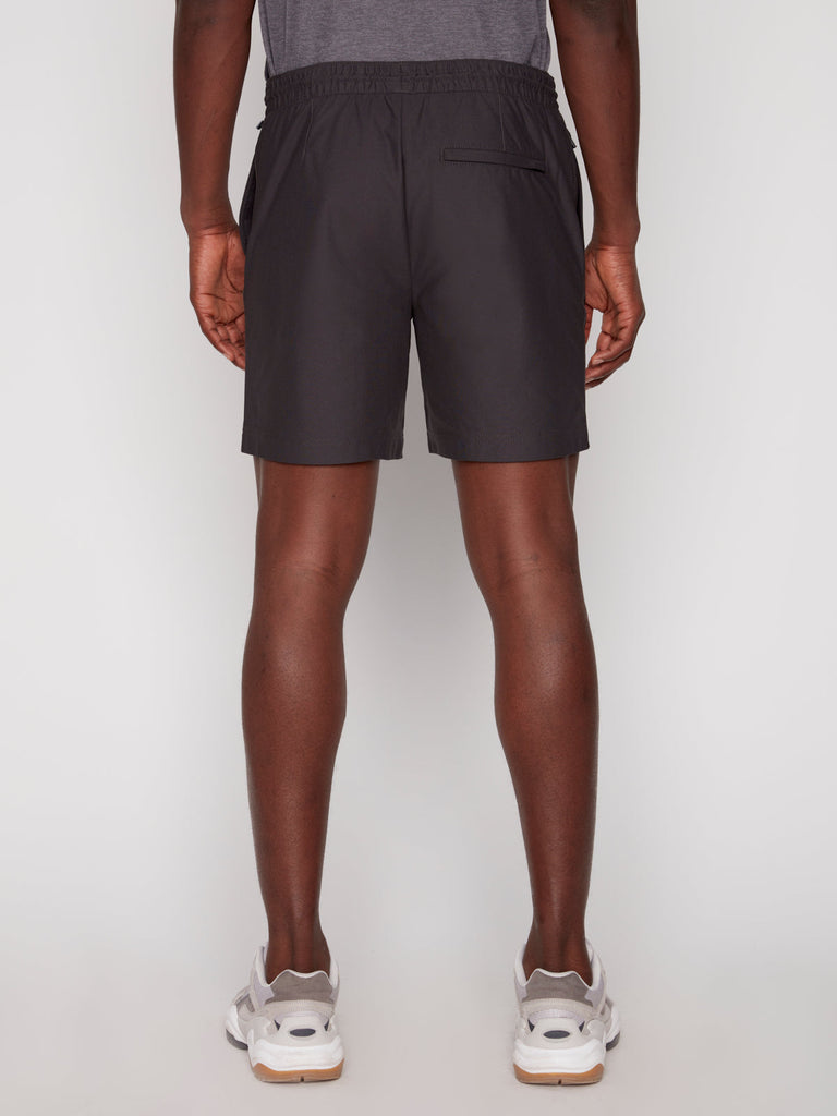 A person faces away from the camera, wearing a gray T-shirt, Projek Raw JULIUS MENS SHORT - CHARCOAL with an elastic waistband and back pocket, and white athletic sneakers.