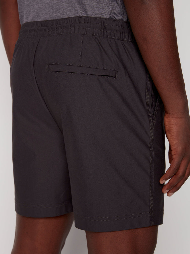 A person wearing Projek Raw JULIUS MENS SHORT - CHARCOAL, featuring an elastic waistband and a single back welt pocket, is seen from the back (waist down) with their right hand resting by their side.