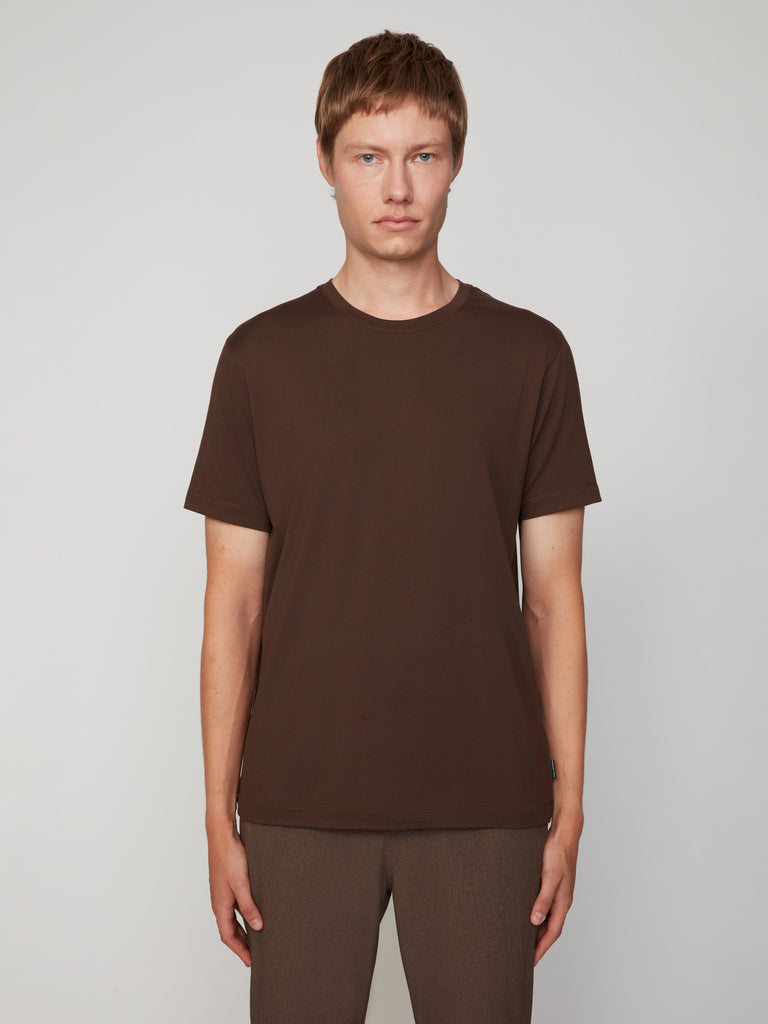 A person with short light brown hair wears the TECH APPAREL MEN’S PEACH:TECH CLASSIC FIT CREW NECK T-SHIRT and brown pants, standing against a light gray background, looking directly at the camera with a neutral expression.