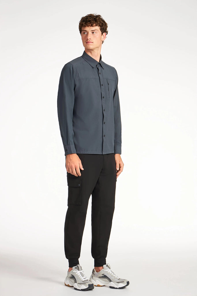 A young man in a dark gray button-up shirt, TECH APPAREL MENS FLUX 2.0 CARGO JOGGER, and white chunky sneakers stands against a plain white background, looking slightly to the side with a neutral expression.