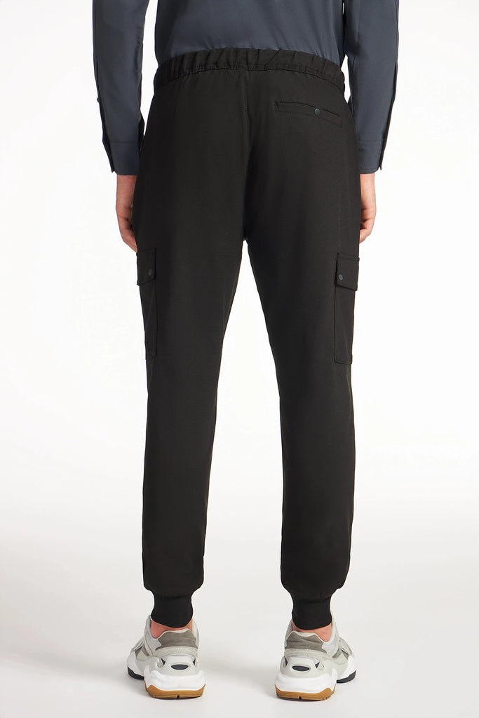 A person faces away wearing TECH APPAREL MENS FLUX 2.0 CARGO JOGGER, crafted from stretch flux fabric with cuffed ankles and side pockets. White sneakers finish this modern mens look against a white background.