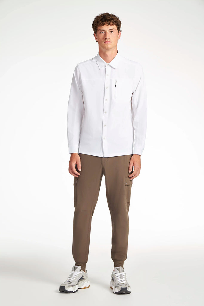 A young man faces forward against a white background, wearing a white button-down shirt, TECH APPAREL MENS FLUX 2.0 CARGO JOGGER in olive green stretch flux fabric, and white sneakers.