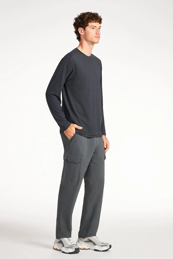 A young man faces right in a dark long-sleeve shirt, TECH APPAREL MENS DRI-FLEX CARGO PANT, and white sneakers against a plain white background.