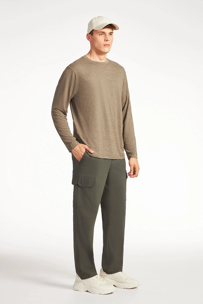 A person stands facing slightly right, one hand in their pocket, wearing a light beige cap, long-sleeve taupe shirt, white sneakers, and TECH APPAREL MENS DRI-FLEX CARGO PANT with utility pockets, against a plain white background.