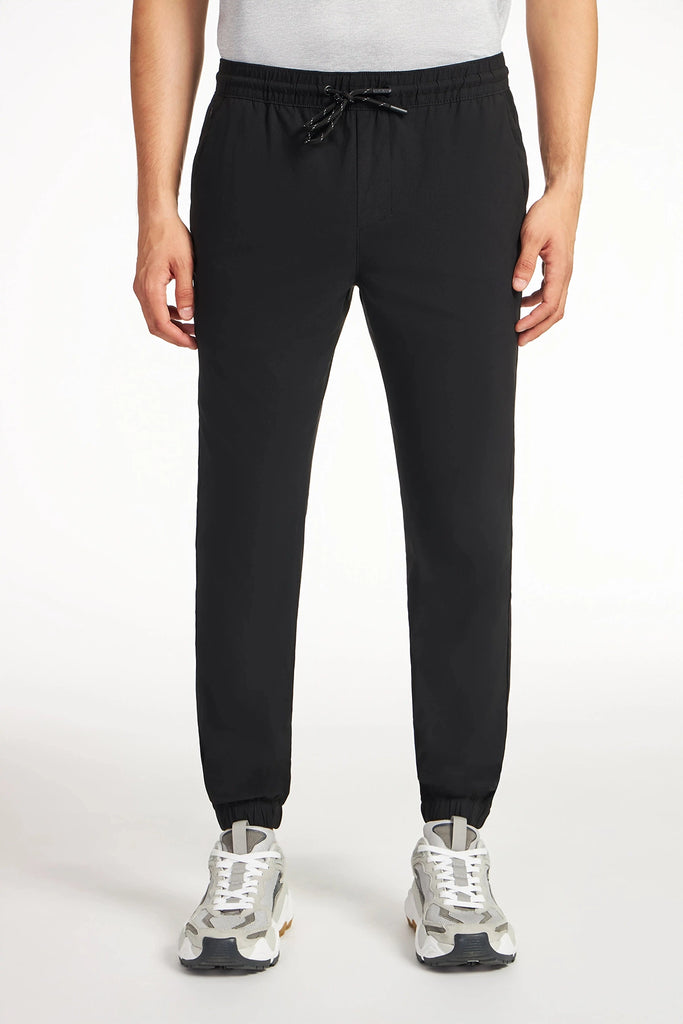 A person wearing a white shirt, TECH APPAREL MENS DRI-FLEX JOGGER pants with an athletic fit and drawstring waist, and gray-and-white sneakers stands against a plain white background.