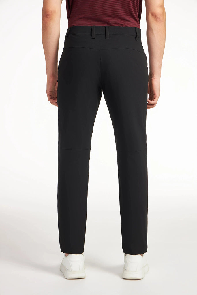 A person faces away from the camera wearing TECH APPAREL MENS DRI-FLEX PANTS in black, a burgundy shirt, and white sneakers against a plain white background.