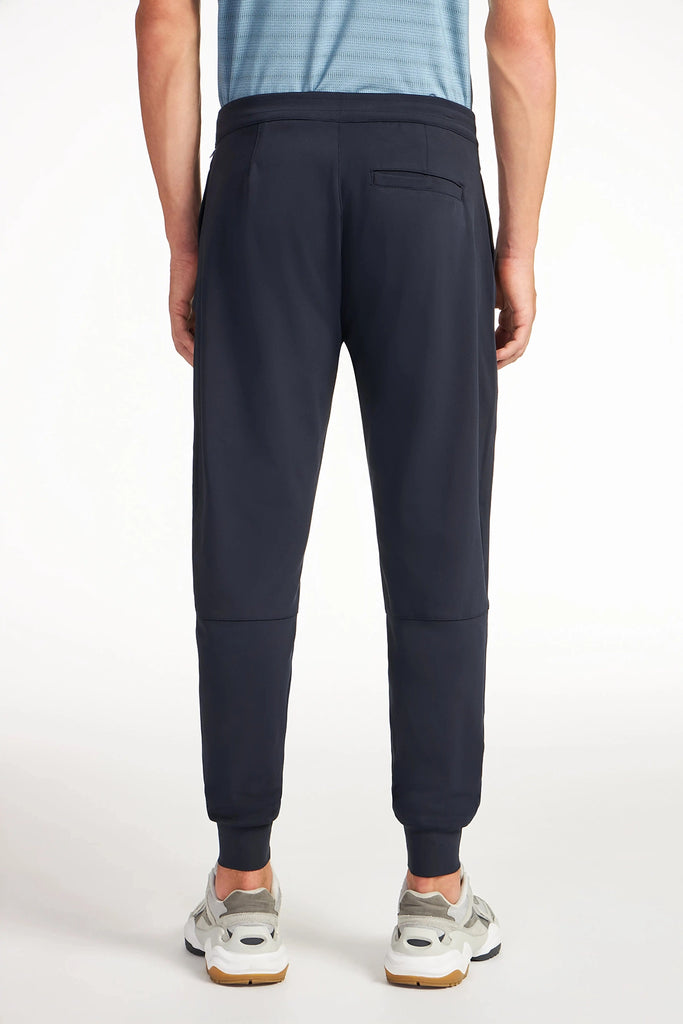 A person wearing a blue striped shirt, TECH APPAREL MENS AERO-KNIT JOGGER, and gray sneakers stands with their back to the camera against a plain white background.