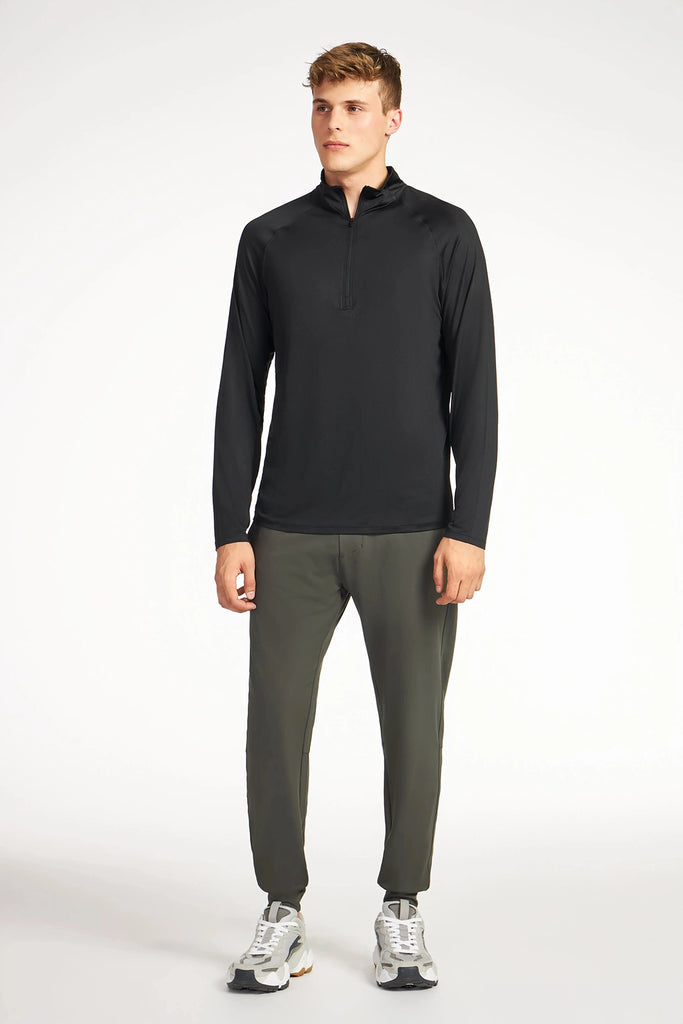 A person stands facing forward against a white background, wearing the TECH APPAREL MENS AERO-KNIT JOGGER crafted from stretch fabric, a black long-sleeve quarter-zip shirt, and white athletic shoes.