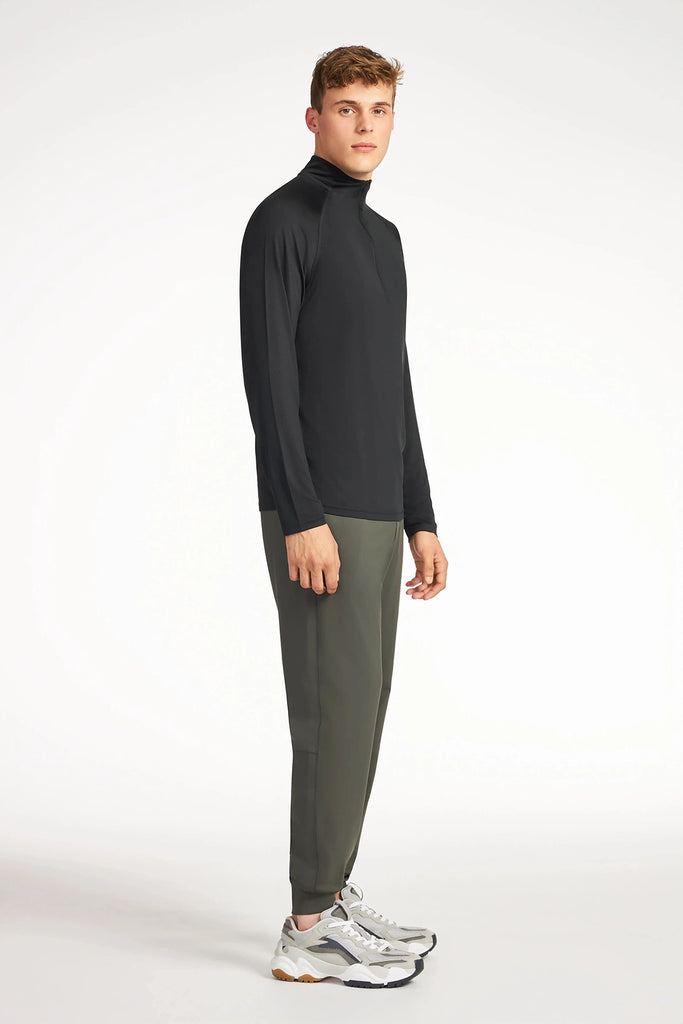 A young man stands slightly angled, wearing a black long-sleeve turtleneck, TECH APPAREL MENS AERO-KNIT JOGGER, and white sneakers against a plain white background.