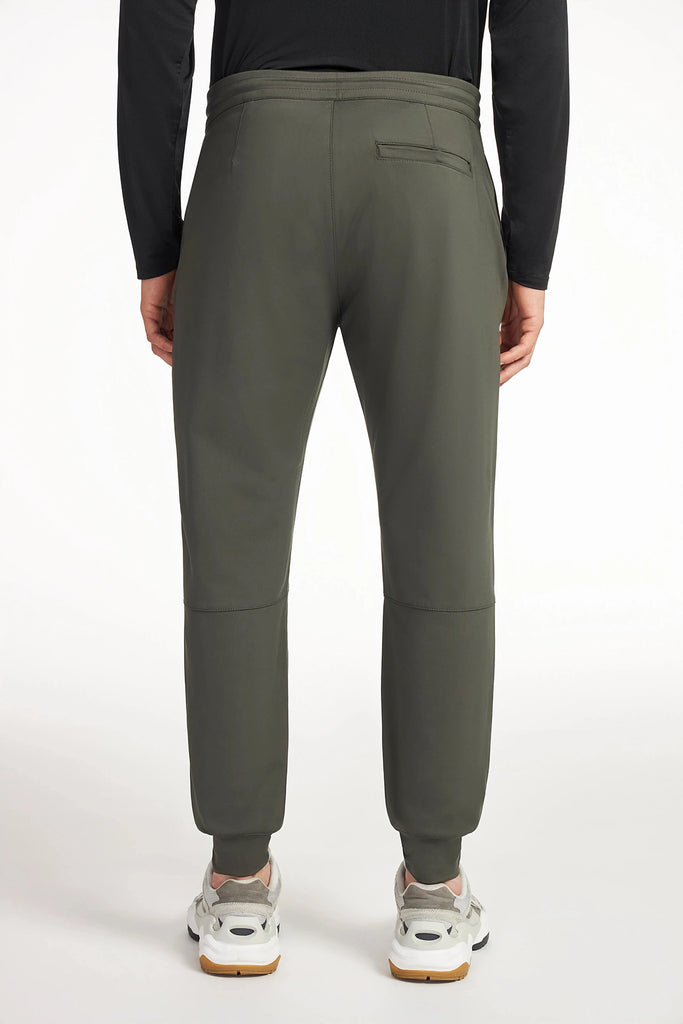 A person stands with their back to the camera against a white background, wearing TECH APPARELs MENS AERO-KNIT JOGGER in olive green, a black long-sleeve shirt, and white athletic shoes.