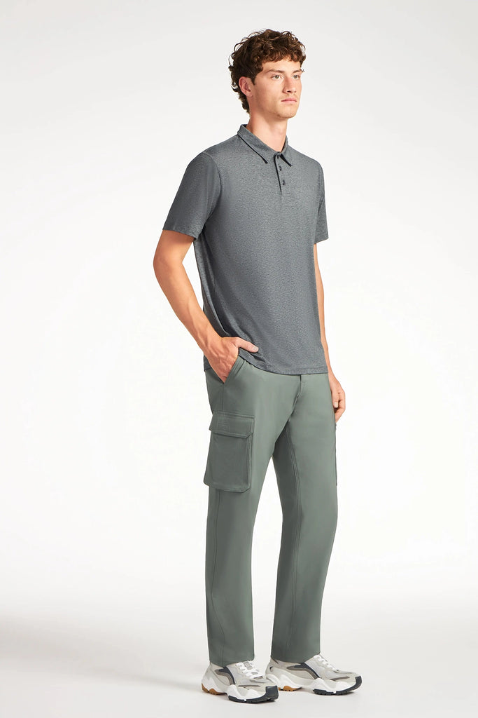 A young man stands with one hand in his pocket, wearing a short-sleeve gray polo shirt, TECH APPAREL MENS THERMAL FLEX UTILITY PANT, and white sneakers against a plain white background.