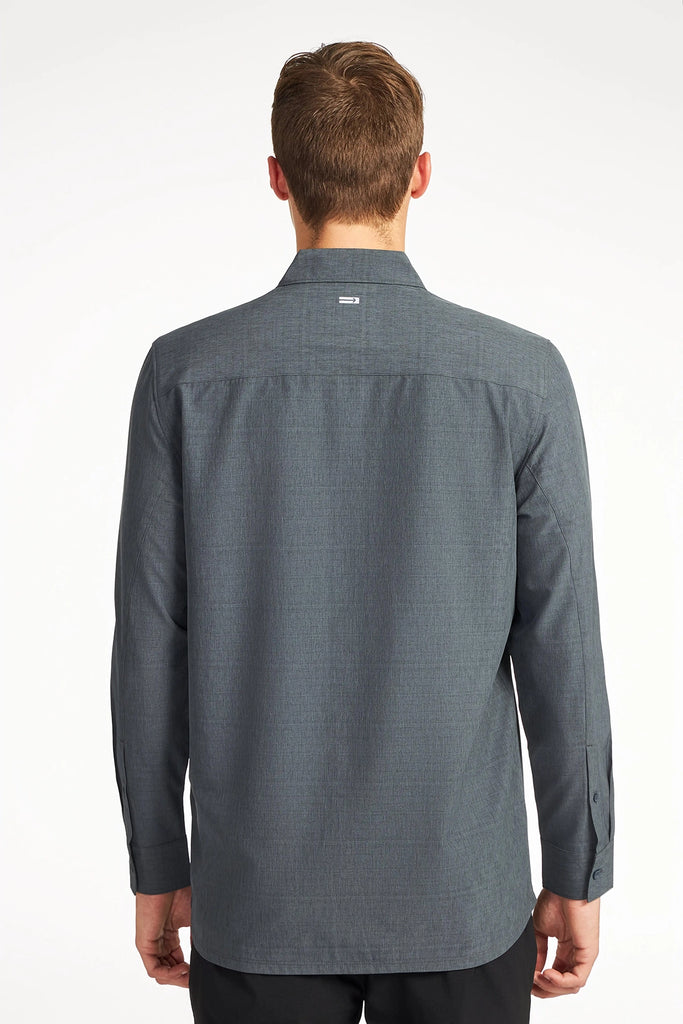 A man with short light brown hair is shown from behind, wearing the TECH APPAREL MENS FOUR WAY STRETCH SHIRT in dark gray and black pants against a plain white background.