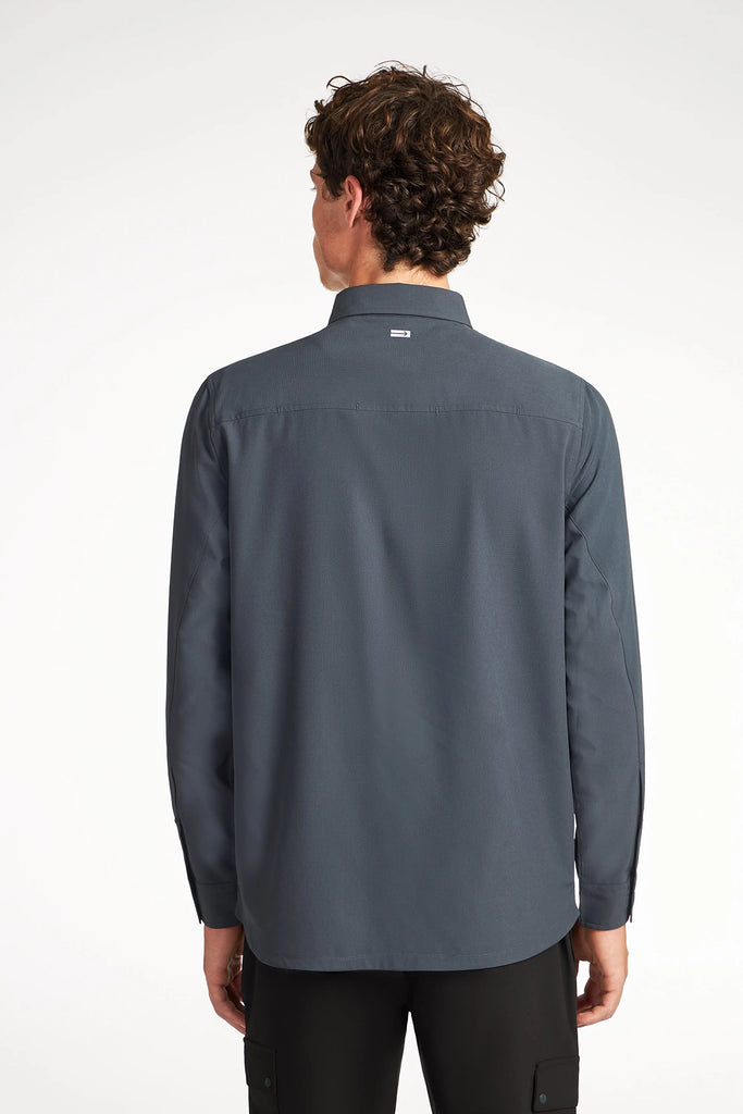 A man with curly brown hair is seen from behind, wearing the TECH APPAREL MENS SOLID STRETCH RIPSTOP SHIRT and black pants, standing against a plain white background.