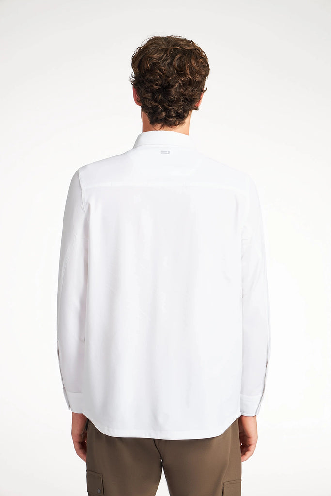 A person with short curly hair is seen from behind, wearing the TECH APPAREL MENS SOLID STRETCH RIPSTOP SHIRT and brown pants, standing against a plain white background.