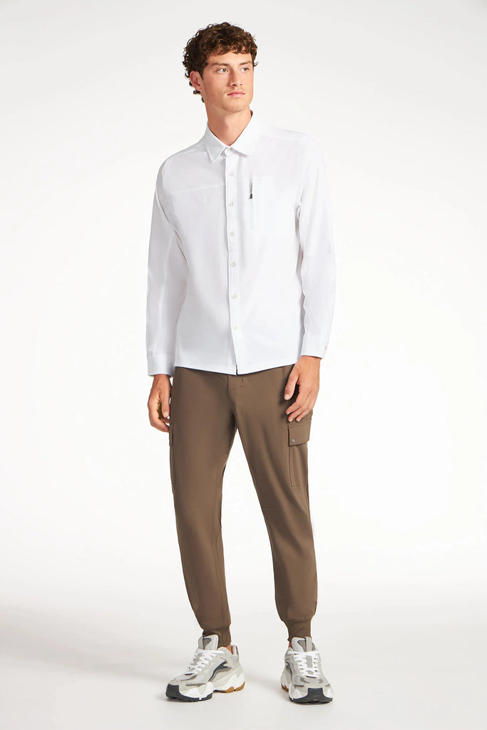 A young man wears the TECH APPAREL MENS SOLID STRETCH RIPSTOP SHIRT, brown cargo joggers, and white sneakers against a white background, looking slightly to the side with a neutral expression.