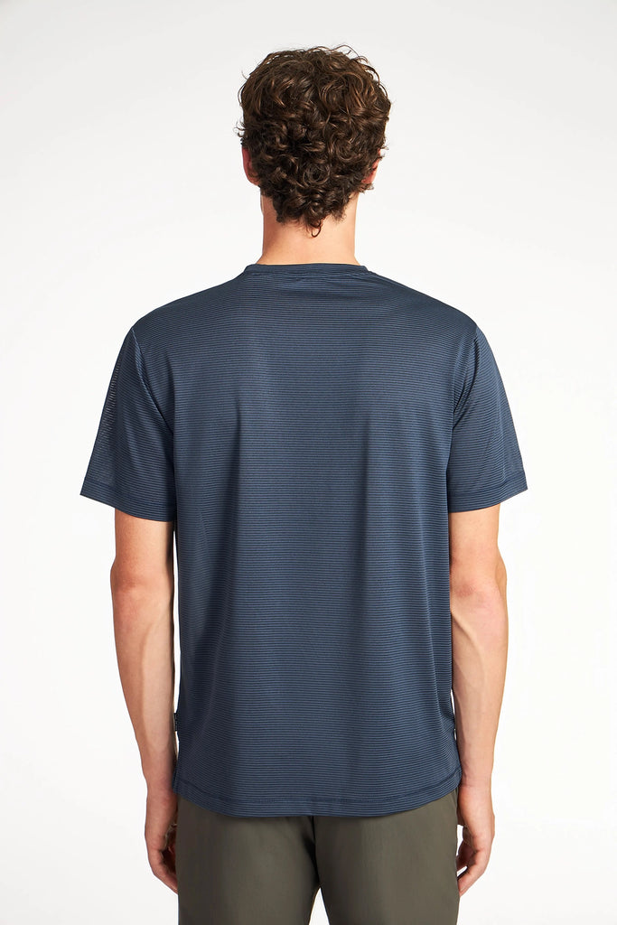 A person with short curly hair faces away from the camera, wearing the TECH APPAREL MENS VARIEGATED STRIPE CREWNECK T-SHIRT and olive-green pants against a plain white background.