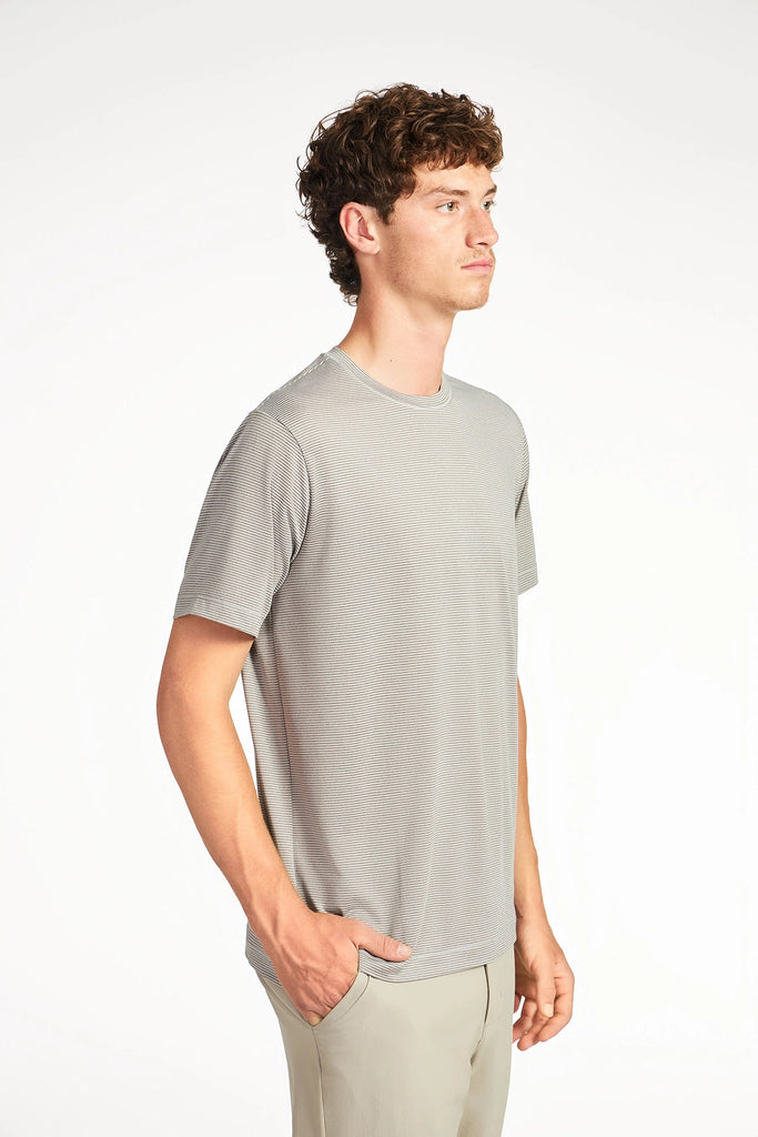 A young man with curly brown hair stands slightly to the right, wearing a light gray TECH APPAREL MENS VARIEGATED STRIPE CREWNECK T-SHIRT and matching pants, one hand in his pocket. The background is plain white.