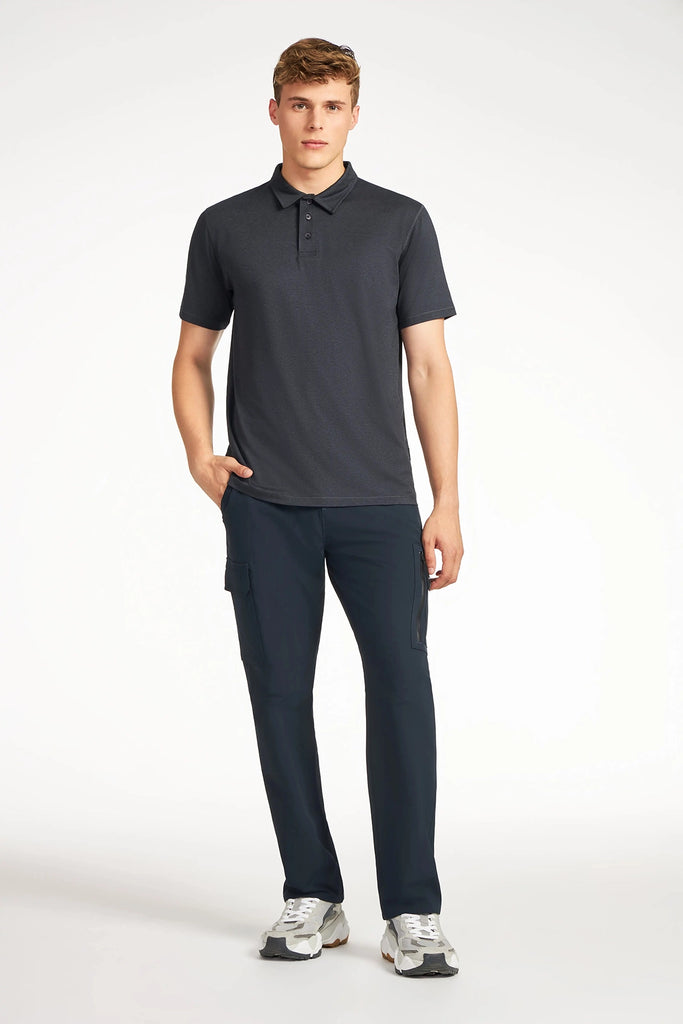 A young man stands against a white background in a wrinkle-resistant TECH APPAREL MENS BRUSHED SPACE DYED POLO, dark cargo pants, and gray sneakers. He looks slightly to the side with one hand in his pocket.