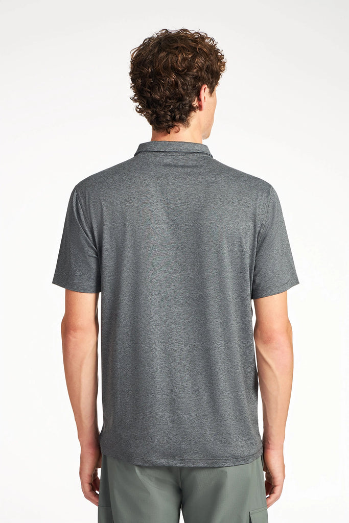 A man with short curly hair stands with his back to the camera, wearing a TECH APPAREL MENS BRUSHED SPACE DYED POLO in dark gray and light gray shorts against a plain white background.