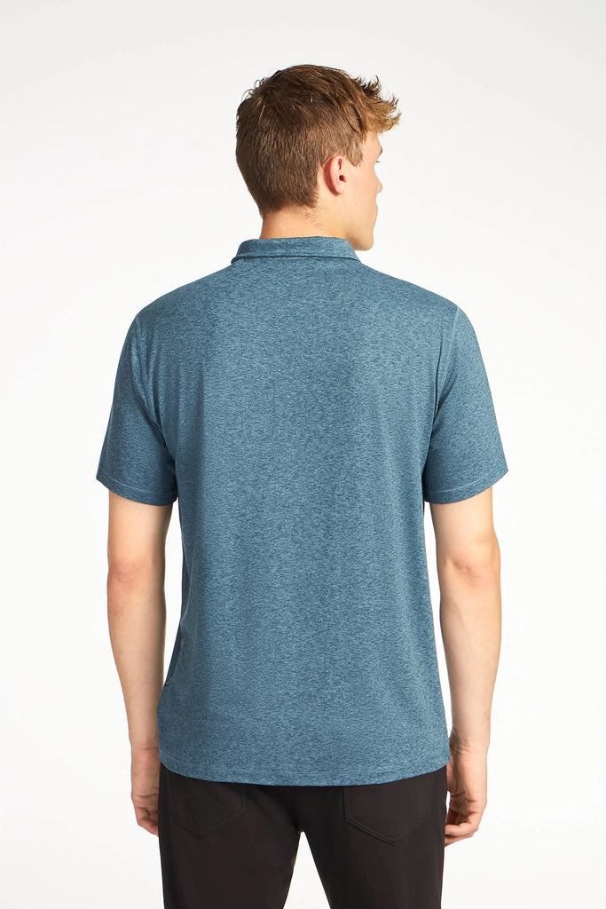 A man with short, light brown hair stands with his back to the camera, wearing TECH APPARELs MENS BRUSHED SPACE DYED POLO and black pants against a plain white background.