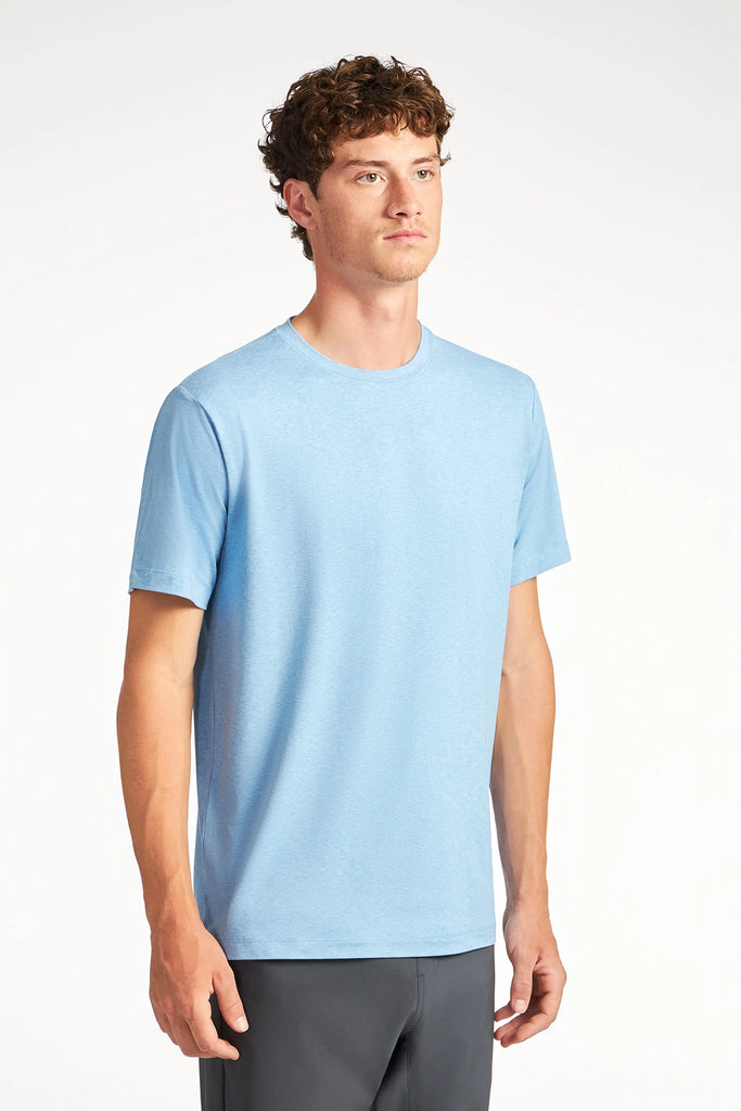 A young man with short curly hair wears the TECH APPAREL MENS BRUSHED SPACE DYED T-SHIRT and dark pants, standing against a plain white background and looking slightly to the side.