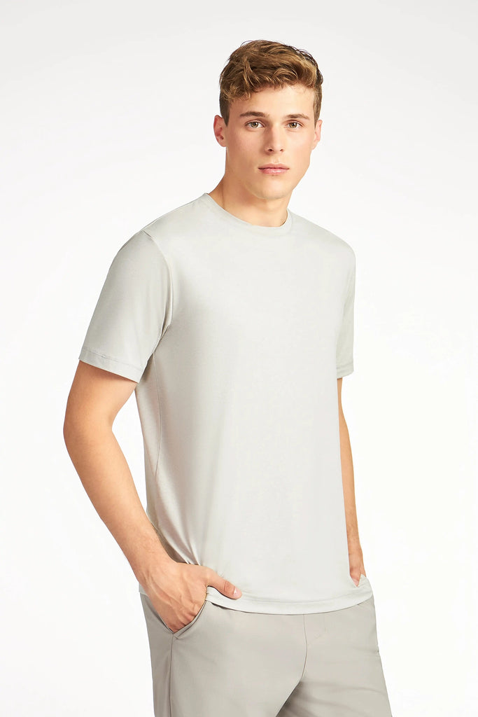 A young man with short, light brown hair wears the TECH APPAREL MENS BRUSHED SPACE DYED T-SHIRT and matching pants, standing with one hand in his pocket against a plain white background.