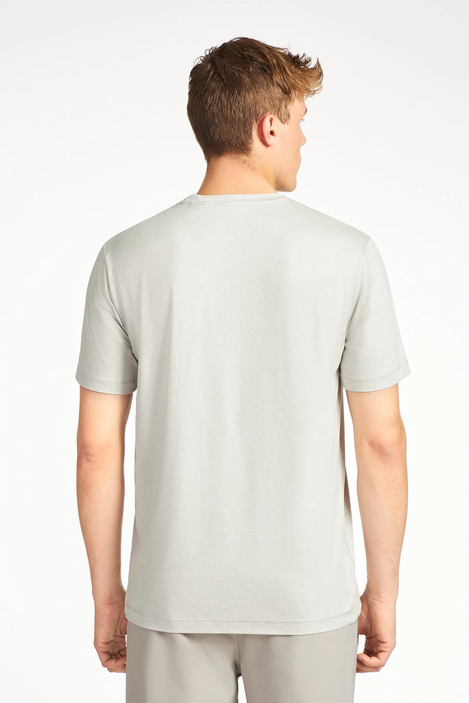 A man with short light brown hair stands with his back to the camera, wearing a TECH APPAREL MENS BRUSHED SPACE DYED T-SHIRT and matching light gray pants, both in wrinkle-resistant stretch fabric, against a plain white background.
