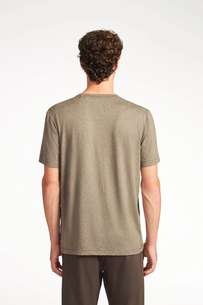 A man with short curly hair, seen from behind, wears the TECH APPAREL MENS BRUSHED SPACE DYED T-SHIRT in light brown and dark pants—a wrinkle-resistant pick for active wear against a plain white background.