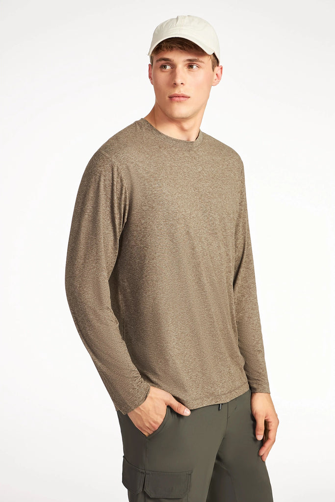 A young man in a wrinkle-resistant TECH APPAREL MENS BRUSHED SPACE DYE LONG SLEEVE TOP, light beige baseball cap, and dark green cargo pants stands with one hand in his pocket, looking off to the side against a white background.