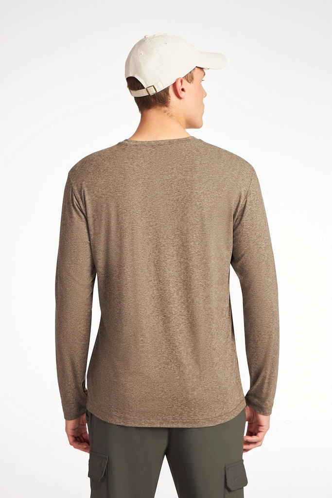 A man stands with his back to the camera against a plain white background, wearing a light beige baseball cap, dark cargo pants, and the TECH APPAREL MENS BRUSHED SPACE DYE LONG SLEEVE TOP in brown.