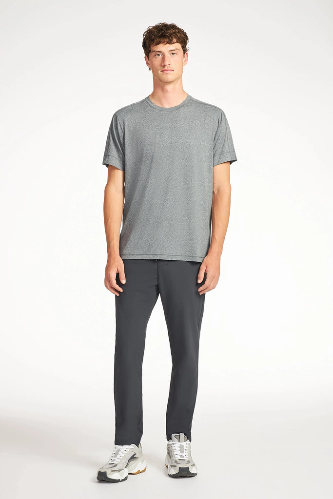 A young man stands against a white background, wearing the TECH APPAREL MENS BRUSHED MARLED T-SHIRT in gray with dark pants and white sneakers. He faces forward with a neutral expression and relaxed posture.