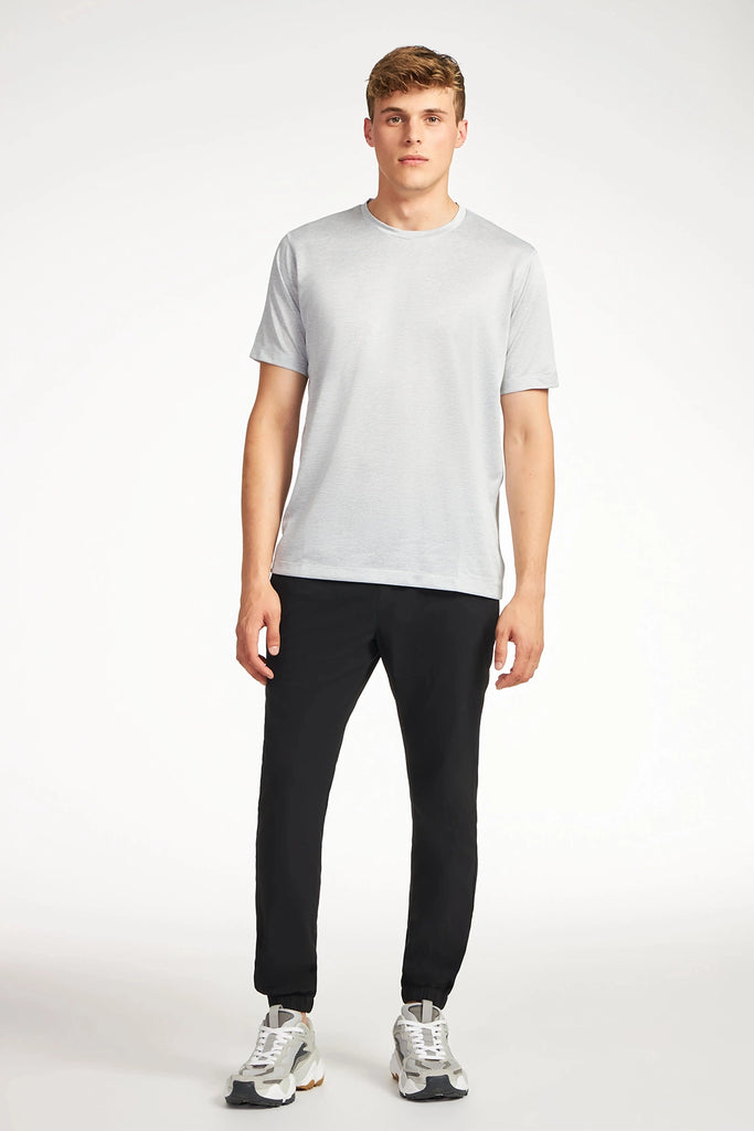 A young man stands facing forward, wearing the TECH APPAREL MENS MARLED PIQUEE T-SHIRT in light gray, paired with black pants and white sneakers against a plain white background.