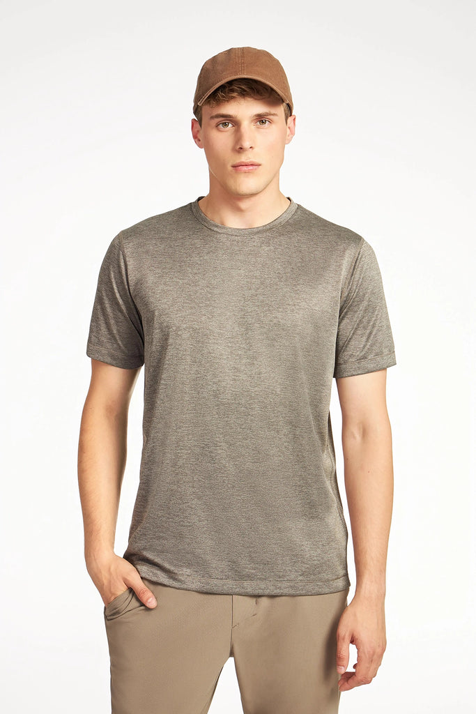 A young man in a TECH APPAREL MENS MARLED PIQUEE T-SHIRT and beige pants stands against a plain white background, wearing a brown cap and looking straight ahead with one hand in his pocket.