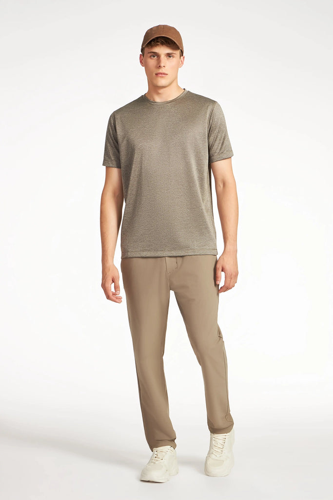 A young man faces forward against a white background, wearing the TECH APPAREL MENS MARLED PIQUEE T-SHIRT, a brown baseball cap, tan pants, and white sneakers.