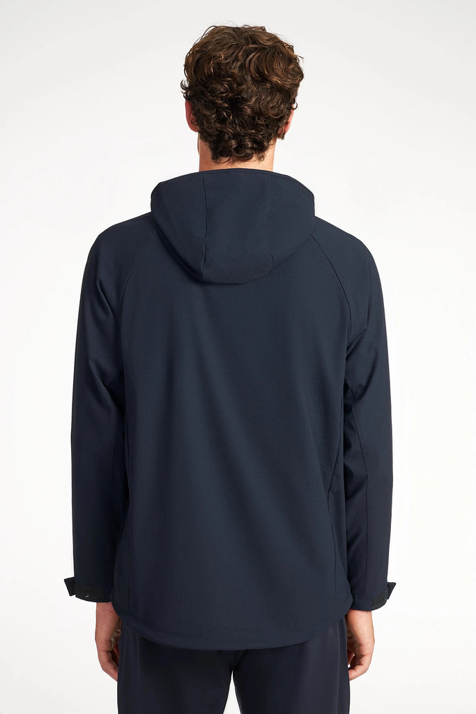 A person with short, curly brown hair is shown from behind wearing the TECH APPAREL MENS DRI-FLEX JACKET and dark pants against a plain, light background.