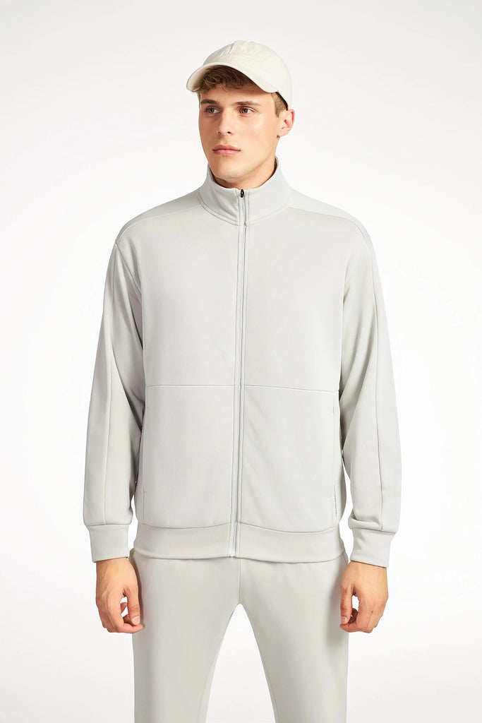 A young man in a light gray TECH APPAREL MENS NEO-KNIT ZIP-UP MOCK NECK SWEATER, matching pants, and a beige baseball cap stands facing forward against a plain white background.