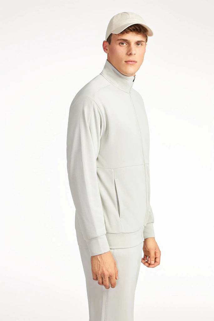 A young man in a light gray TECH APPAREL MENS NEO-KNIT ZIP-UP MOCK NECK SWEATER and matching cap stands slightly turned against a white background, highlighting sleek TECH APPAREL style.