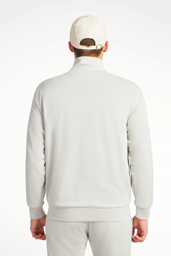 A man in a light beige TECH APPAREL MENS NEO-KNIT ZIP-UP MOCK NECK SWEATER, matching pants, and a baseball cap stands with his back to the camera against a plain white background.