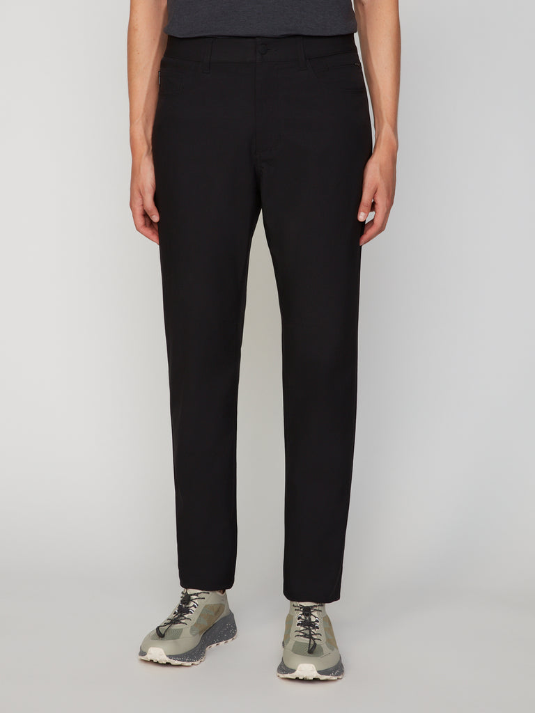 A person models the TECH APPAREL MEN’S 247:TWILL RELAXED TAPERED FIT 5-POCKET PANT with light green sneakers, shown from the waist down against a plain white background.