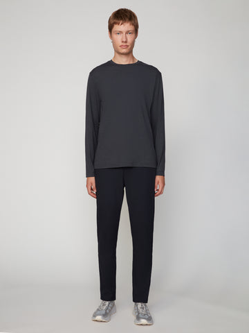 A man stands facing forward against a plain light background, wearing a long-sleeved dark gray shirt, gray sneakers, and TECH APPAREL MEN’S 247:TWILL RELAXED TAPERED FIT 5-POCKET PANT.