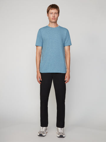 A person stands facing forward against a plain background, wearing a light blue short-sleeve t-shirt, TECH APPAREL MENS PULL-ON CHINO 247:TWILL PANT in black, and gray sneakers.