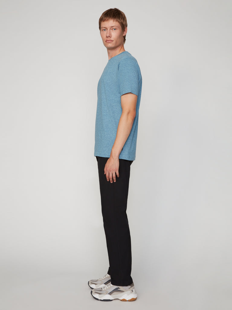A man in profile against a plain background wears a blue short-sleeve t-shirt, TECH APPAREL MENS PULL-ON CHINO 247:TWILL PANT, and white sneakers with gray accents.