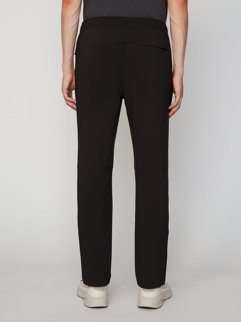 A person faces away from the camera, wearing TECH APPAREL MEN’S PULL-ON TRAINING PANT, RELAXED TAPERED FIT, and light sneakers against a plain background—showcasing athletic versatility.